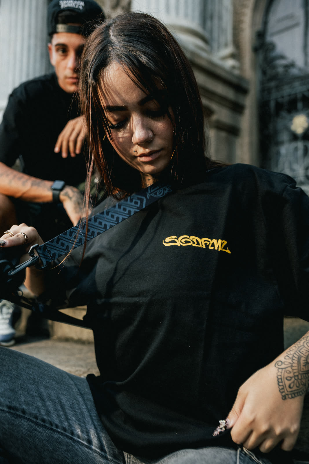 Retrato em close de modelo com camiseta preta e shoulder bag, lettering dourado no peito